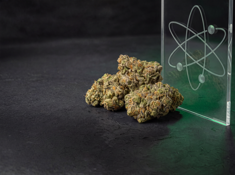 Premium indoor THCA flower buds displayed beside a clear acrylic block with an atom design on a dark textured surface.